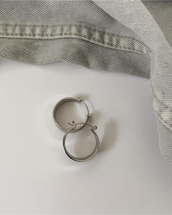 To metaløreringe ligger på en hvid overflade ved siden af en foldet lysgrå denimtekstur.