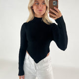 En person tager en selfie i et spejl, iført en sort trøje og hvide bukser. Personen holder en brun telefon, og baggrunden er simpel og lys.