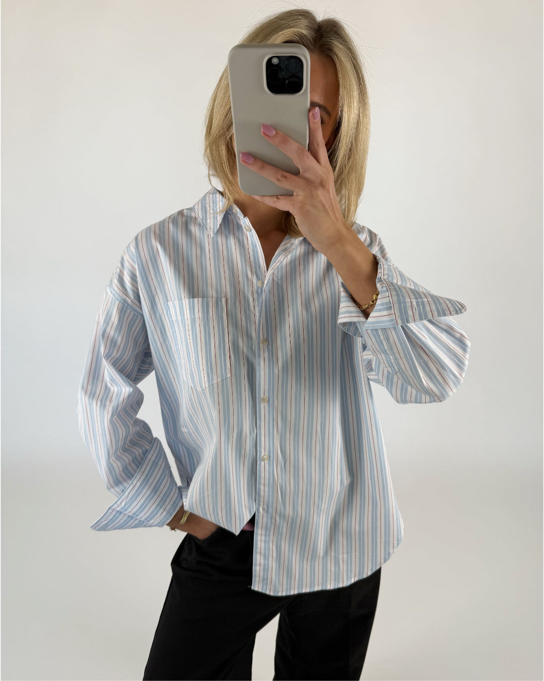 En person i en stribet skjorte holder en smartphone op foran sit ansigt. Konteksten er en lys baggrund.