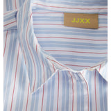 En skjorte med striber i blå og rød ligger fladt med synlig krave. Et mærke indeholder teksten "JJXX". Skjortens mønster er del af et formelt design.