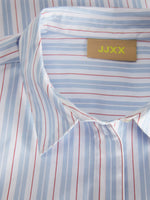 En skjorte med striber i blå og rød ligger fladt med synlig krave. Et mærke indeholder teksten "JJXX". Skjortens mønster er del af et formelt design.