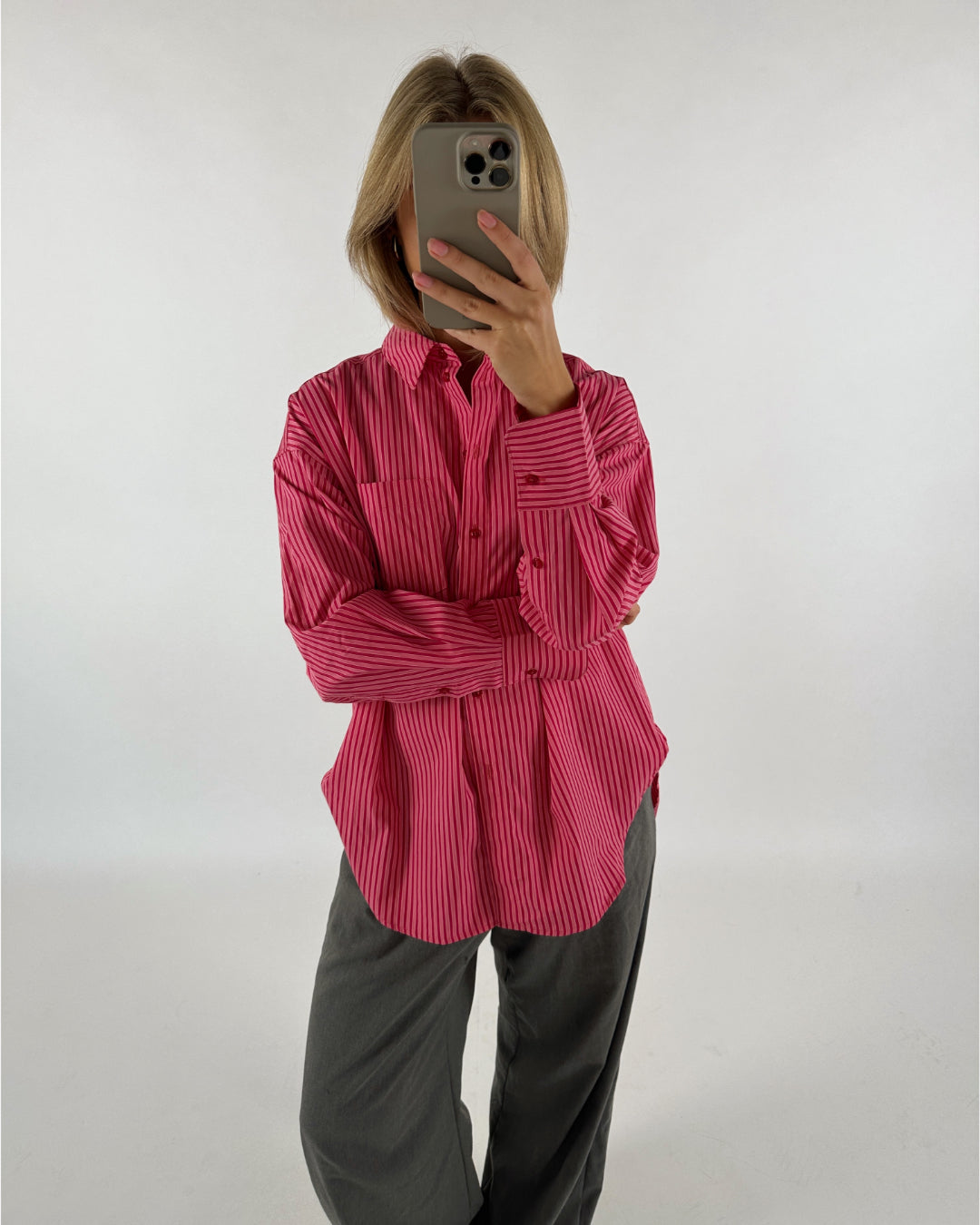Person i en pink stribet skjorte holder en mobiltelefon foran ansigtet. Baggrunden er neutral og hvid.