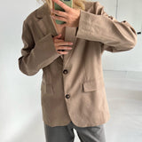 En person i brun jakke tager en selfie med en grøn telefon i et lyst rum. Personen er iført grå bukser og ses fra skuldrene og ned.
