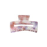 En stor hårklemme i nuancer af pink og lilla marmorering ses på en hvid baggrund. Hårklemmen er åben, klar til brug og skinnende i lyset.