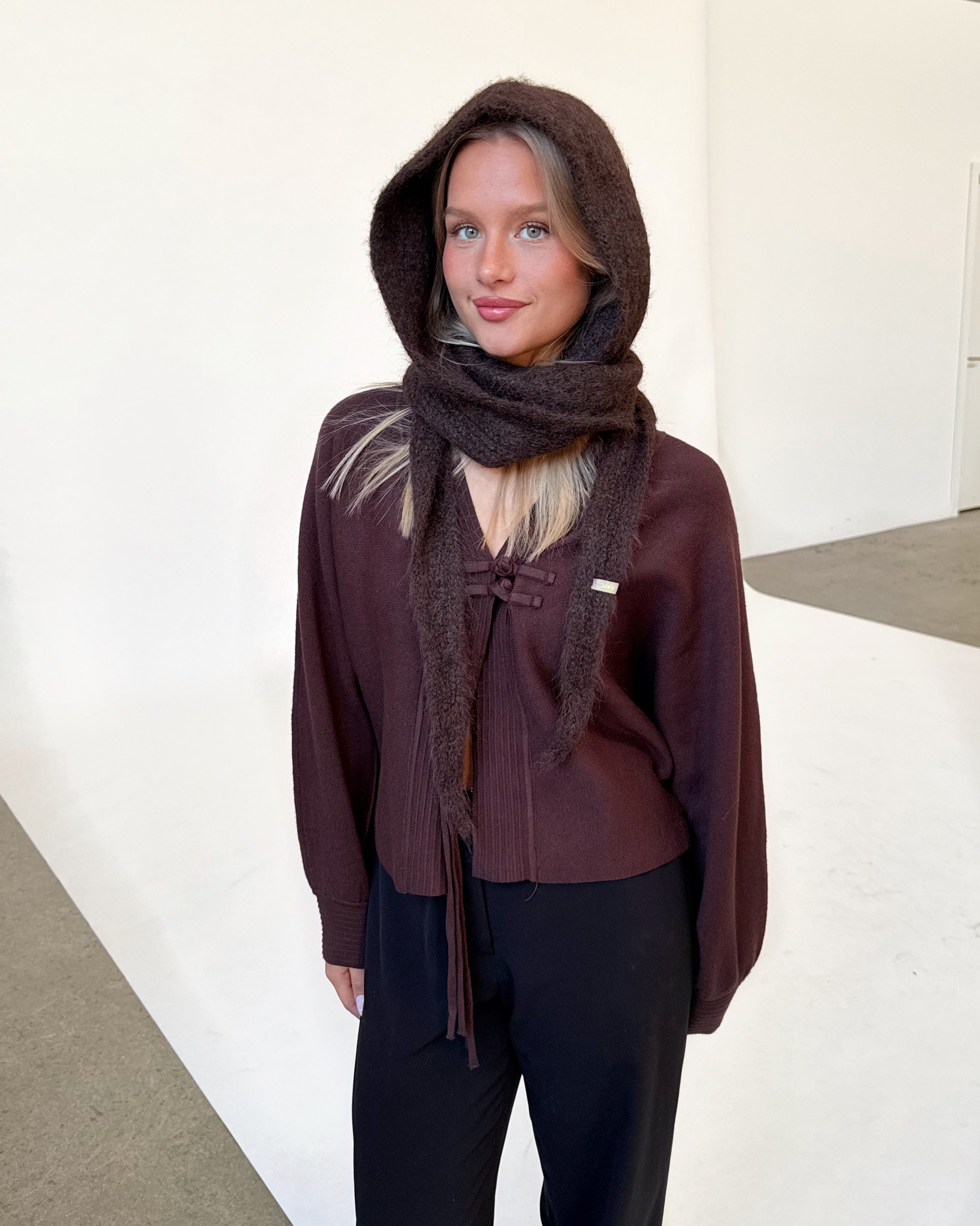 Modelfoto af pige iført brun KATHERINE balaclava, bordeaux cardigan og sortmelerede ELLIS bukser. Alt er fra BySofieSønderby.