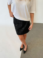 Modelfoto af pige i sort KENDALL nederdel med pailetter, samt hvid basic t-shirt og spidse ballerinaer. Alt er fra BySofieSønderby.