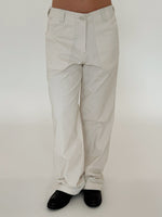 Bukser, iført af en person, er lyse og vide, parret med sorte sko. Baggrunden er enkel og hvid, hvilket fremhæver det minimalistiske look.