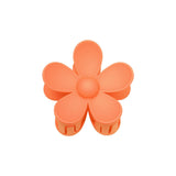 Orange blomstformet hårklemme med seks kronblade, ligger på en hvid baggrund.