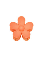 Orange blomstformet hårklemme med seks kronblade, ligger på en hvid baggrund.