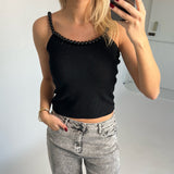 Kvinde iført sort top med perlepynt tager selfie. Hun har lyse jeans og rød neglelak. Baggrund er et lyst indendørs rum.