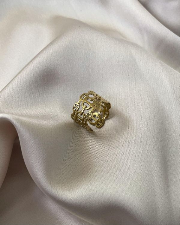 En intrikat guldring ligger stille på krøllet, lysebrunt stof, der giver en elegant og luksuriøs baggrund.