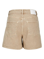 Beige shorts med lommer bagpå står alene mod en hvid baggrund; designet inkluderer en hvid etiket nær taljen.