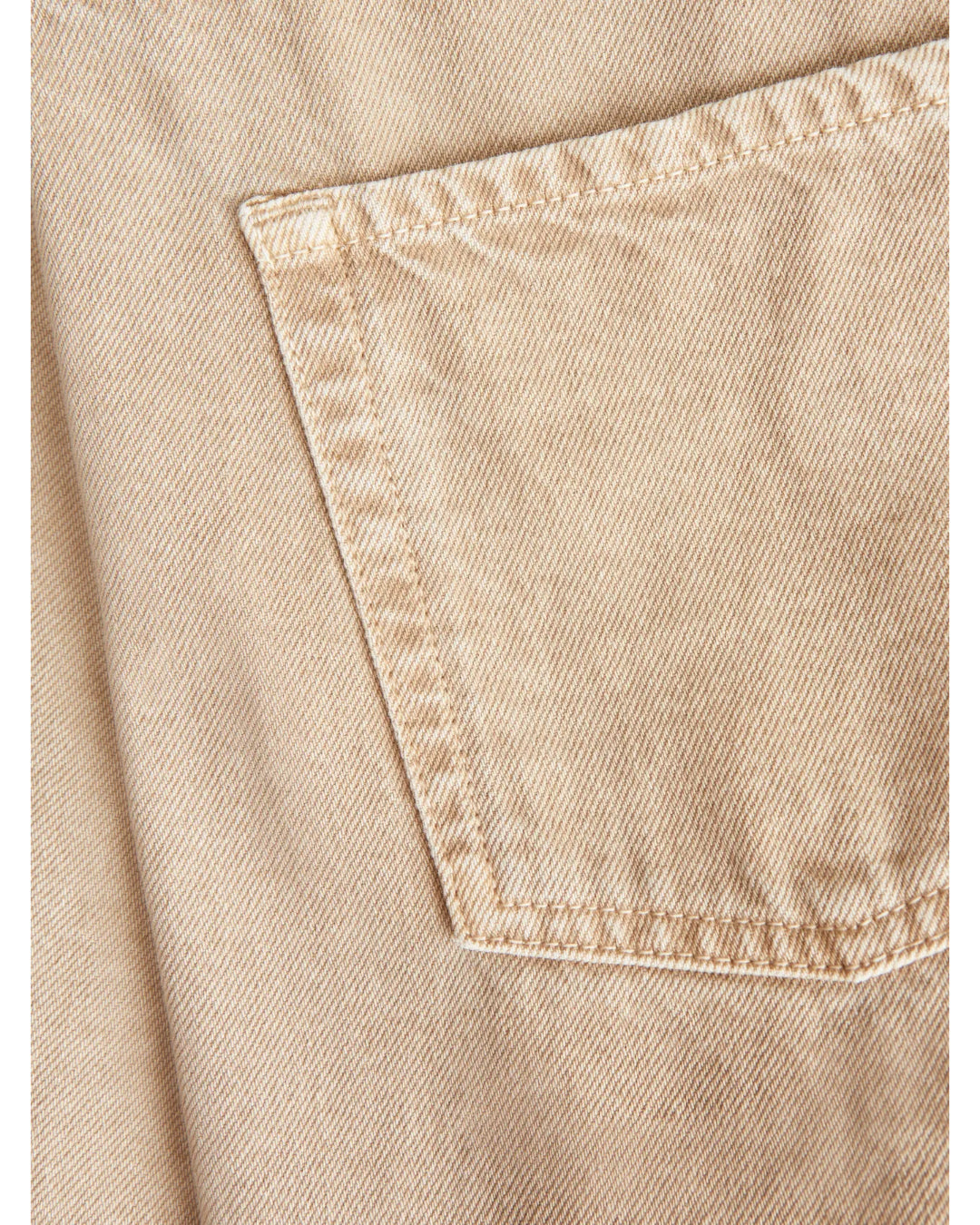 Lomme syet på beigefarvet denimstof, med diagonale syninger. Stoffet er præget af en tæt og ensartet vævning, hvilket skaber et robust og holdbart udseende. Ingen tekst.