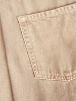 Lomme syet på beigefarvet denimstof, med diagonale syninger. Stoffet er præget af en tæt og ensartet vævning, hvilket skaber et robust og holdbart udseende. Ingen tekst.