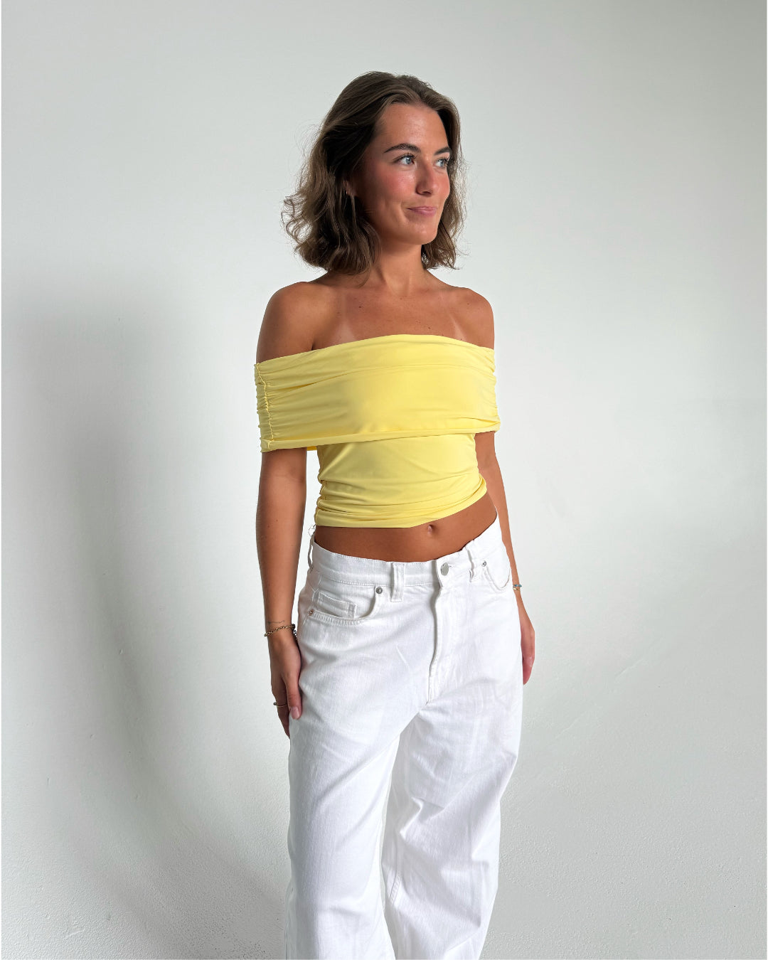 Modelfoto af pige som bærer en Leia top i gul, samt et par hvide Nanna jeans. Alt fra By Sofie Sønderby