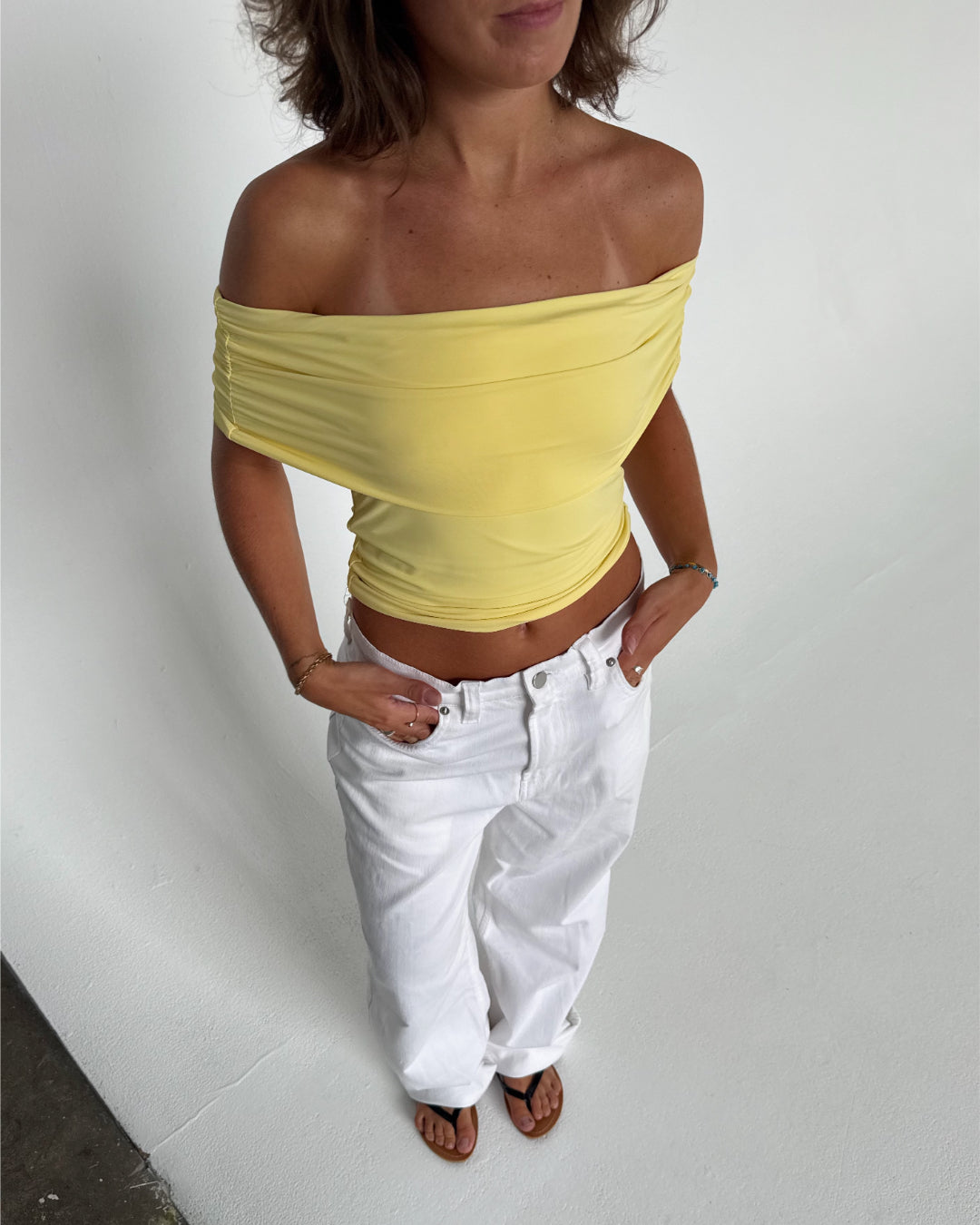 Modelfoto af pige som bærer en Leia top i gul, samt et par hvide Nanna jeans. Alt fra By Sofie Sønderby