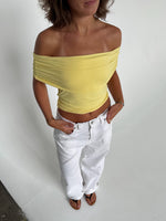 Modelfoto af pige som bærer en Leia top i gul, samt et par hvide Nanna jeans. Alt fra By Sofie Sønderby