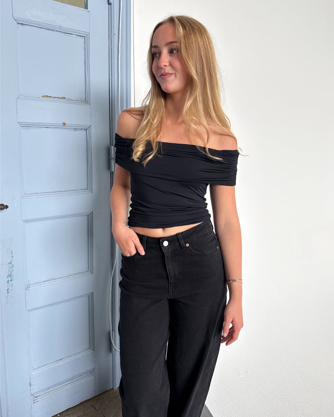 Modelfoto af pige som bærer en Leia top i sort, samt et par hvide Nanna jeans. Alt fra By Sofie Sønderby