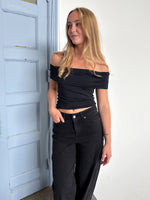Modelfoto af pige som bærer en Leia top i sort, samt et par hvide Nanna jeans. Alt fra By Sofie Sønderby