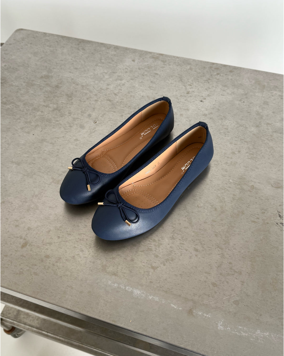 To mørkeblå ballerina-sko med sløjfer er placeret side om side på en grå overflade. Indersålen har mærketext, der siger "ALDO" og "8 UK 41 EUR".