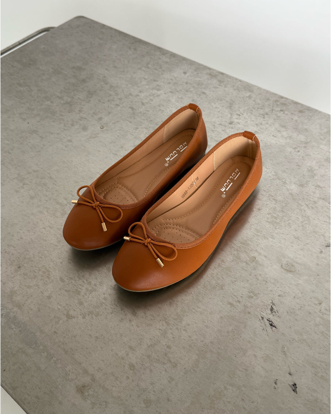 Brune ballerina-sko med sløjfer ligger på en grå bordplade. Indersålen viser teksten: "be luluma 01206" samt "36-38 3-355-5P-0808".