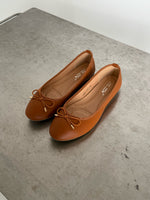 Brune ballerina-sko med sløjfer ligger på en grå bordplade. Indersålen viser teksten: "be luluma 01206" samt "36-38 3-355-5P-0808".