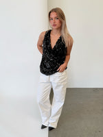 Modelfoto af pige i sort LINA top med pailetter, samt hvide NANNA jeans. Alt er fra BySofieSønderby.