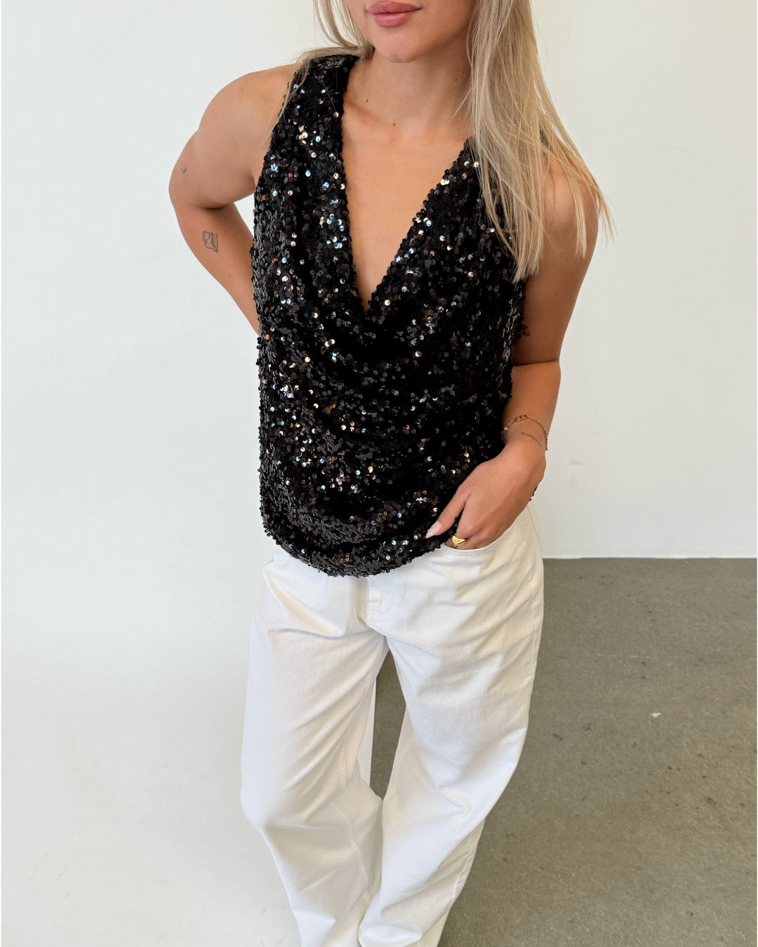 Modelfoto af pige i sort LINA top med pailetter, samt hvide NANNA jeans. Alt er fra BySofieSønderby.