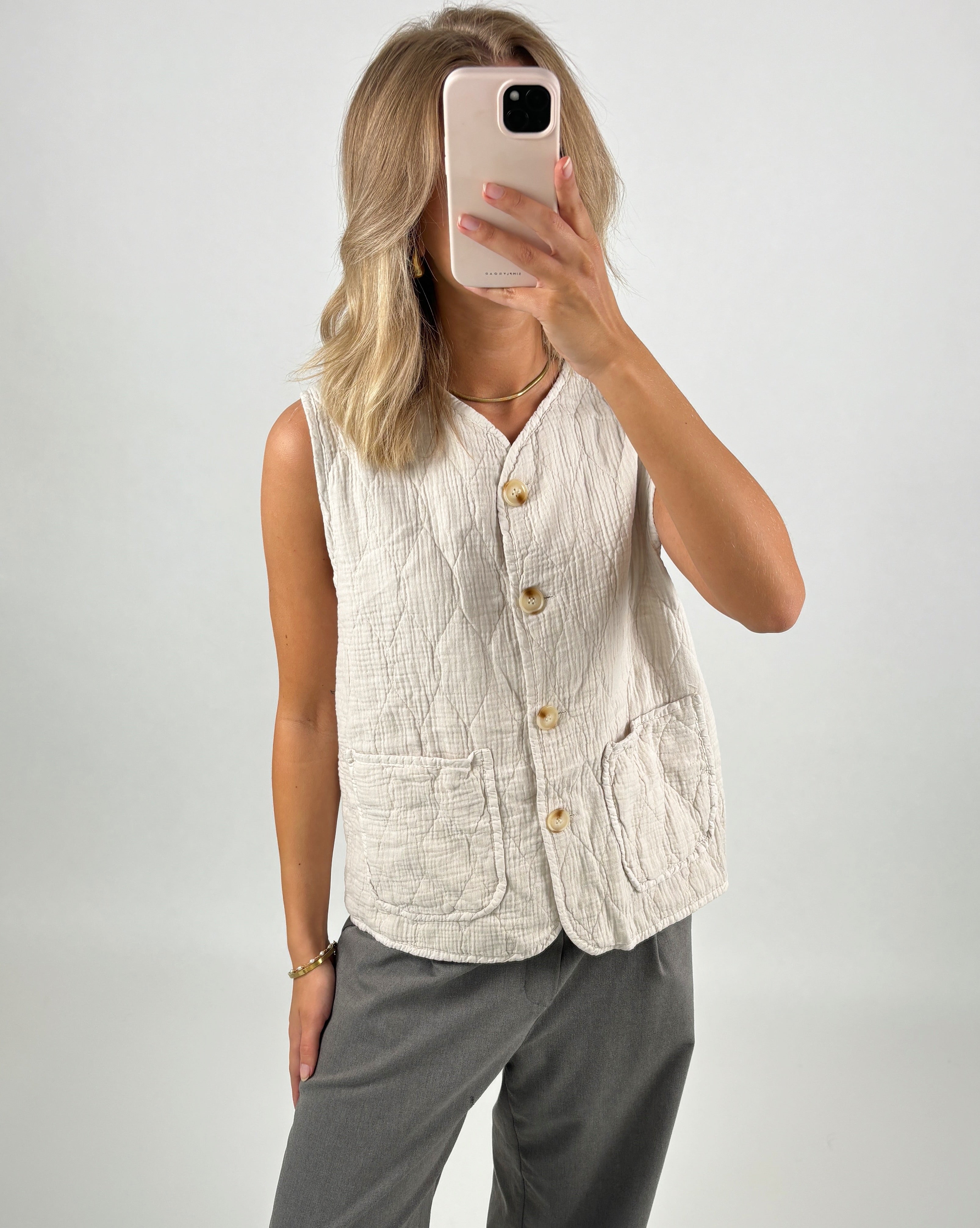En person i en cremefarvet vest tager et spejlbillede med en smartphone. Baggrunden er neutral.