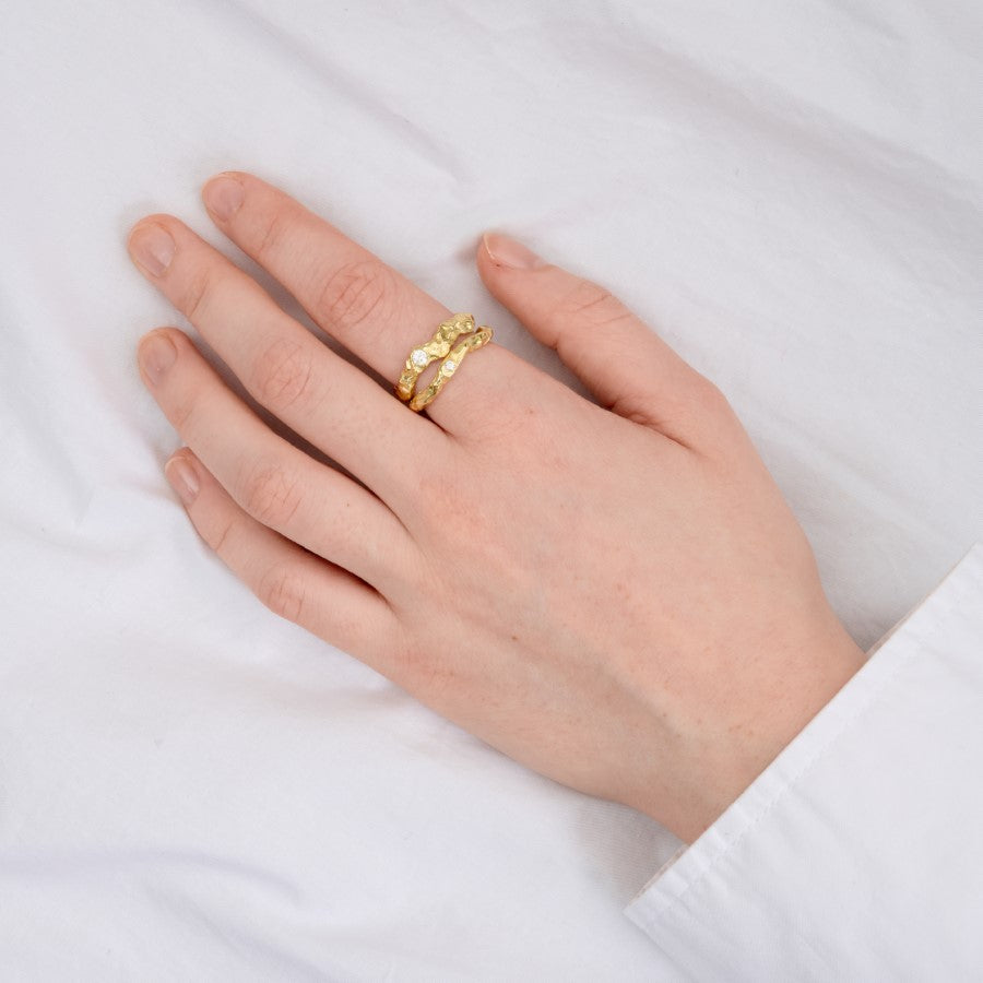 Hånd bærer en gylden ring med tekstur på fjerde finger, mens hånden hviler på en hvid overflade, skaber en elegant og enkel scene.