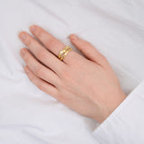 Hånd bærer en gylden ring med tekstur på fjerde finger, mens hånden hviler på en hvid overflade, skaber en elegant og enkel scene.