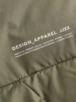 Grønt stof med trykt tekst: "DESIGN_APPAREL JJXX ENERGETIC/VIBRANT/SOCIAL/DEDICATED/STRONG/AIM HIGH PREMIUM QUALITY WOMENSWEAR APPAREL // LONDON STUDIOS".