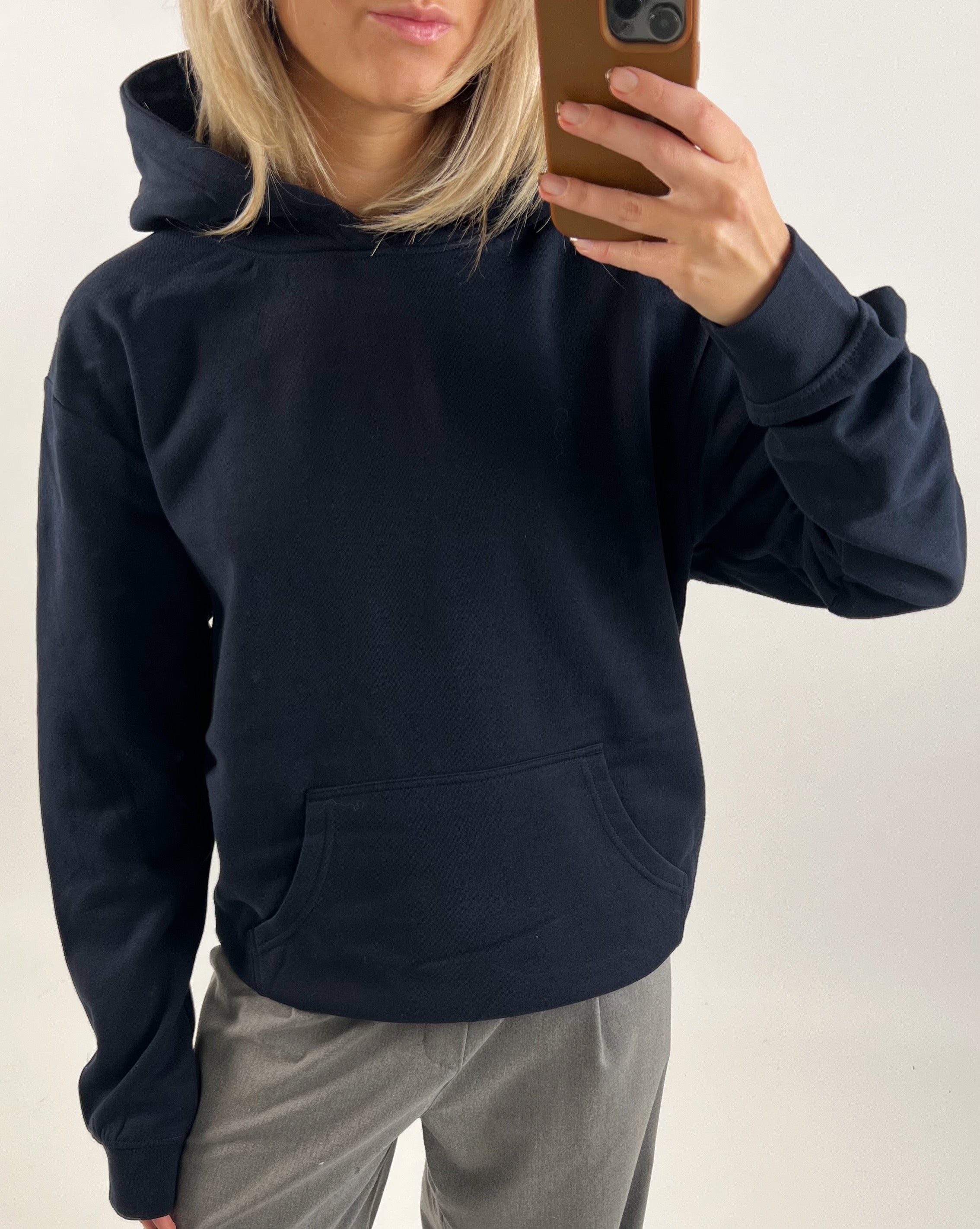 En person i en sort hættetrøje tager et spejlfoto med en brun mobiltelefon. Personen står i et uformelt interiørmiljø uden yderligere genstande synlige.