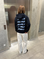 Stemningsbillede af pige der bærer en navy hoodie med blåt LOS ANGELES tryk og hvide NANNA jeans.  Fra BySofieSønderby