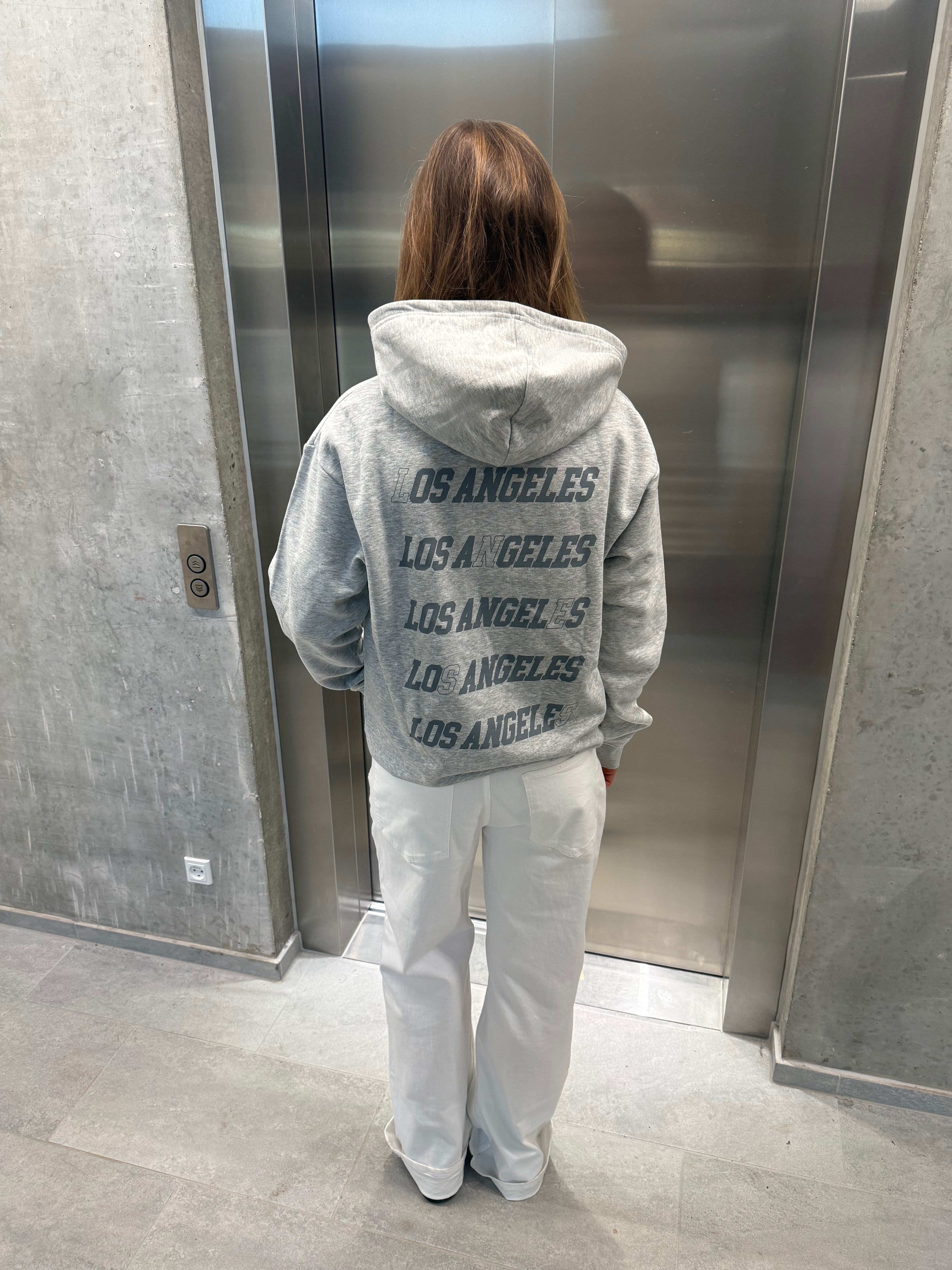 Stemningsbillede af pige der bærer en grå hoodie med gråt LOS ANGELES tryk og hvide NANNA jeans.  Fra BySofieSønderby