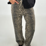Bukser med leopardprint bæres af en person, der hviler en hånd i lommen. Personen har sorte sko og en sort overdel. Baggrunden er neutral og lys.