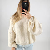 En person iført en hvid, strikket sweater holder en mobiltelefon med sort cover foran ansigtet; personen har lange, lyse lokker, og neglene er rødmalede. Baggrund er ensfarvet lys.
