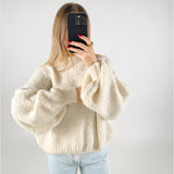 Person tager et billede med en smartphone, iført en stor, lys sweater. Personen har løst, langt hår og røde negle. Baggrunden er en simpel, hvid væg.