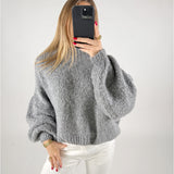 En person iført en grå sweater tager en selfie med en sort smartphone. Personen har hvidt tøj på og rød neglelak. Baggrunden er ensfarvet hvid.