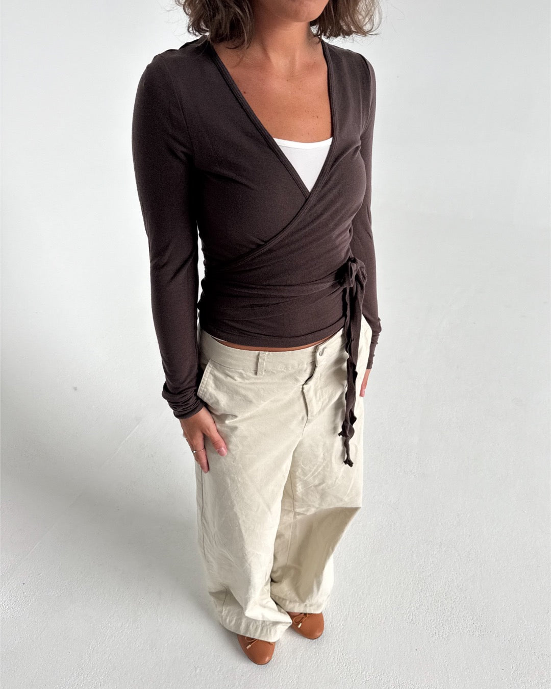 Modelfoto af pige i brun Luna wrapbluse og beige bukser. Fra BySofieSønderby