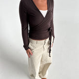 Modelfoto af pige i brun Luna wrapbluse og beige bukser. Fra BySofieSønderby