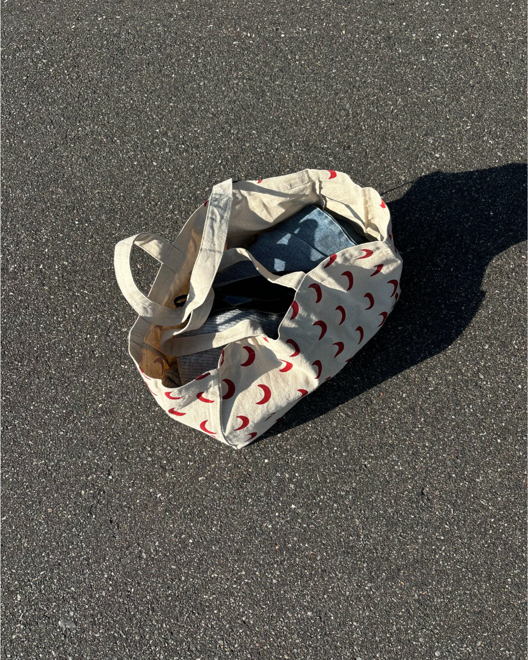 Et stofnet med røde halvmåne-motiver ligger åbent på en asfalteret vej i sollys, indeholdende tøj eller lignende genstande.