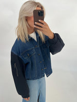 Kvinne i cowboyjakke tager et selfie, står i et neutralt rum. Hun har lyst hår og en mobiltelefon dækker hendes ansigt delvist. Ingen yderligere tekst eller detaljer i baggrunden.