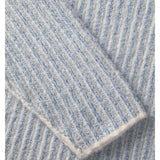En sweater med lys blå og hvid striber ligger foldet. Teksturen er ribstrikket, hvilket giver en blød, varm fornemmelse. Den ligger fladt uden synlige baggrundselementer.