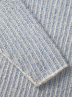 En sweater med lys blå og hvid striber ligger foldet. Teksturen er ribstrikket, hvilket giver en blød, varm fornemmelse. Den ligger fladt uden synlige baggrundselementer.