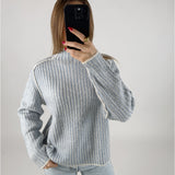 Person iført en stribet sweater og lyse jeans tager et billede med en sort telefon foran sig, i et lyst, neutralt rum.