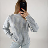 En person iført en lyseblå, stribet sweater tager et billede med en sort telefon. Personen er omgivet af en lys, neutralt farvet baggrund.