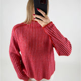 En person iført en rød- og pinkstribet sweater tager et spejlbillede med en sort mobiltelefon. Personen har rød neglelak og bærer en ring. Baggrunden er enkel og lys.