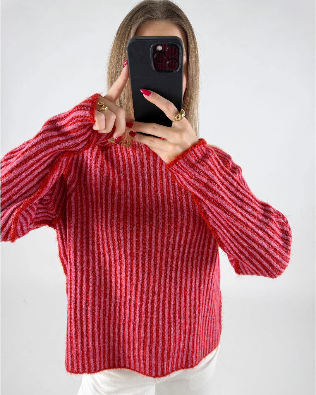 En person holder en sort telefon op foran ansigtet iført en rødstribet sweater, omgivet af en lys baggrund. Personen viser pegefingeren på telefonens skærm.