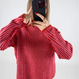 En person holder en sort telefon op foran ansigtet iført en rødstribet sweater, omgivet af en lys baggrund. Personen viser pegefingeren på telefonens skærm.